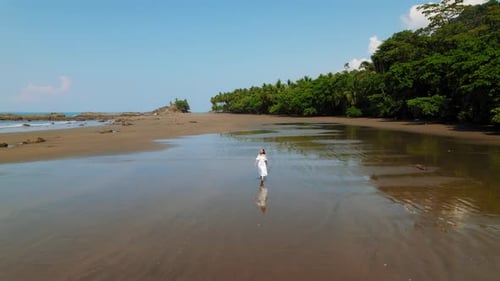 Young woman walks across reflective wet sand on a sunny Costa Rica beach at low tide