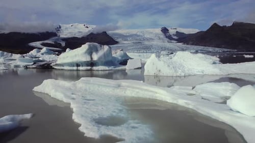 Aerial flying over dramatic icebergs floating in water, Jokulsarlon lake, natural climate snow lands