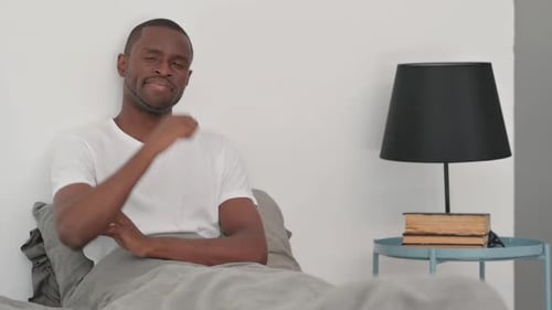Homme africain faisant les pouces en l'air alors qu'il est allongé sur le ventre dans son lit
