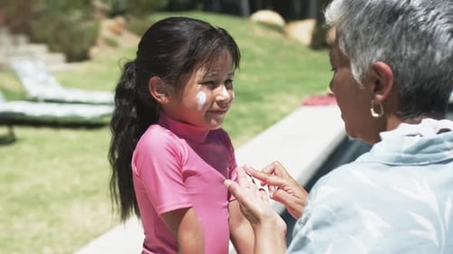 Biracial man applies sunscreen on a biracial girl's face outdoors