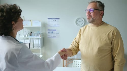 Smiling Patient Talking and Shaking Hands with Doctor in Clinic