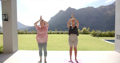 Practicing yoga, two women standing on yoga mats outdoors in mountain setting