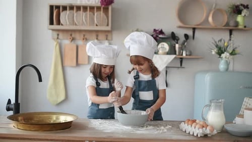 Zwei Kinder in weißer Kochuniform mischen Mehl in einer Schüssel in der Küche