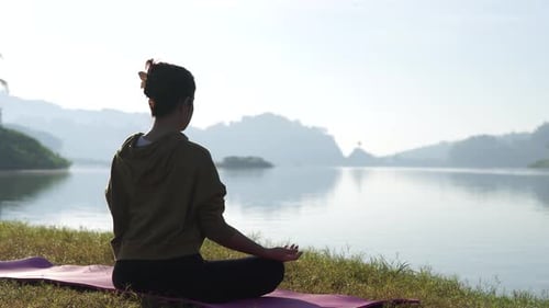 Beautiful young Asian woman practicing yoga by the lake on a quiet and peaceful morning.