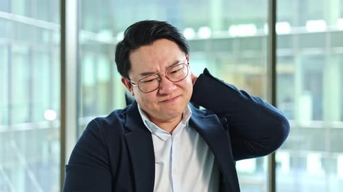 Stressed Businessman with Neck Pain in a Modern Office