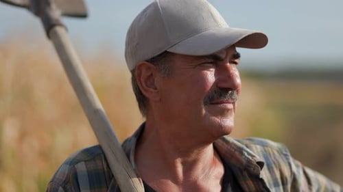Portrait of Senior Farmer with Shovel on Rural Path Next to Fields