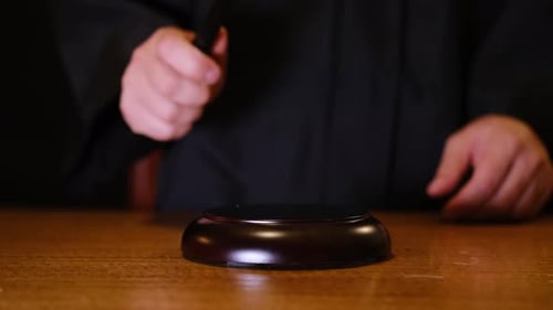 Closeup of a Judge Hand Striking a Wooden Gavel on a Sound Block in a Courtroom Setting