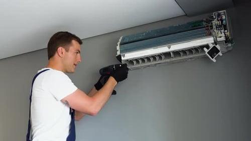 Man Maintaining Air Conditioner with Drill Indoors