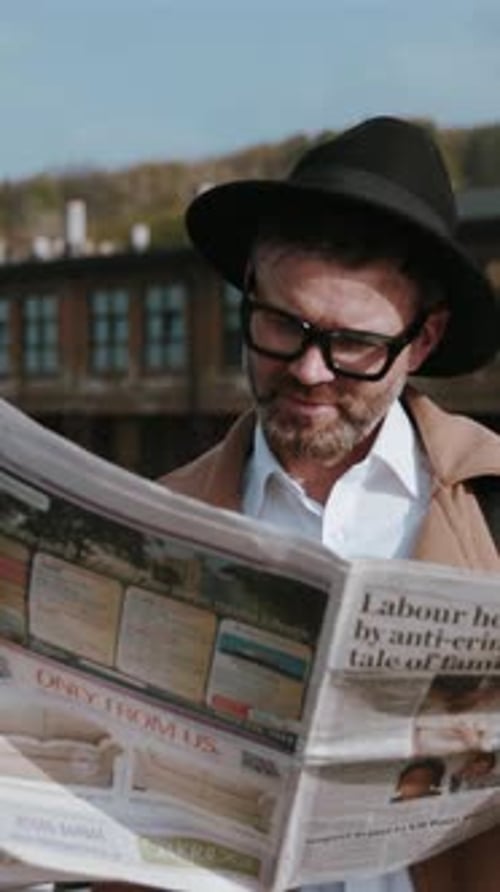 A Stylish and Trendy Man Enjoys Reading a Newspaper Outdoors While Dressed in Chic Attire