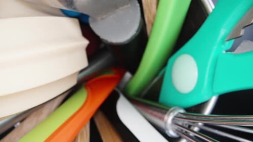 A glass with kitchen utensils, spatulas, scissors and a whisk, top view. Dolly slider extreme close-