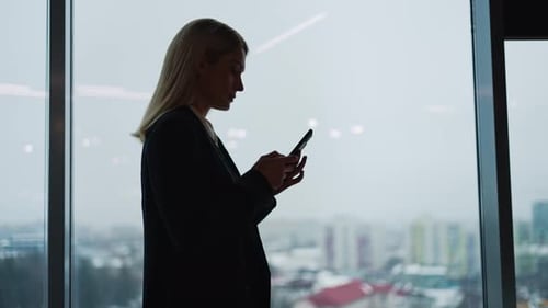 Woman Using Phone By Large Office Window