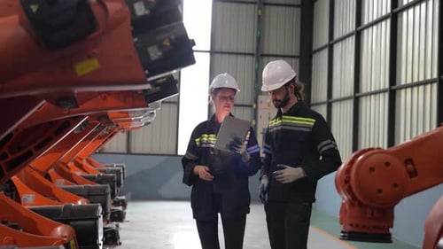 Une technicienne programme un bras robotique avec une tablette numérique et un robot d'assemblage dans une usine.
