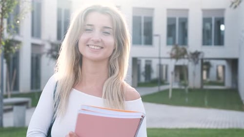 Cheerful Young Blond Woman Holding Book on University Campus