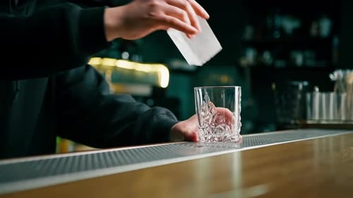 Close up of bartender putting crystal ice cubes in glass while preparing alcoholic cocktail