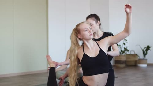 Woman Performs Yoga Pose in a Fitness Club an Instructor Helps Her Front View