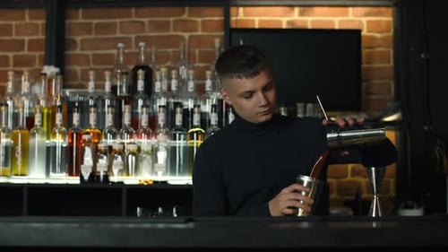 The process of preparing an alcoholic cocktail at the bar. Media. Young male bartender at work