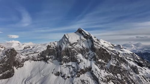 Aerial view of the snow-covered Fronalpstock peak with rugged cliffs and a clear blue sky in Glarus