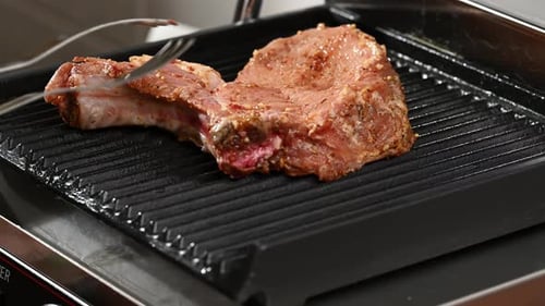 Raw piece of pork hand puts with tongs on the grill