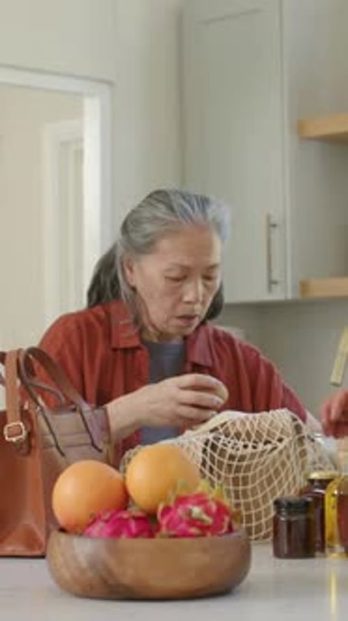 Vídeo vertical: Colocando el bolso, la bolsa de malla hacia abajo, una mujer con la parte superior oxidada desempacando en el mostrador, embolsando frascos