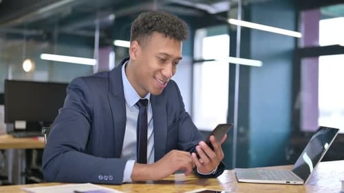 Man Smiles While Using Mobile Phone in Office