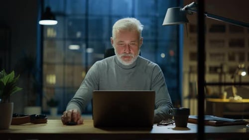 Senior man working at desk in office at night