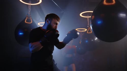 Brutal Caucasian Strong Male Boxer Punching Bag in Gym