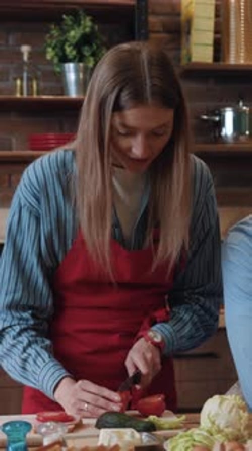 Woman Slicing Vegetables in Kitchen with Friend