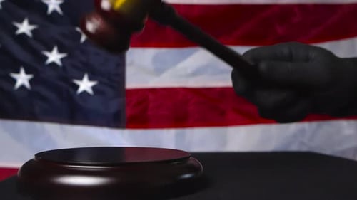 El juez golpea con la mano un martillo judicial frente a una bandera de los Estados Unidos de América en cámara lenta.