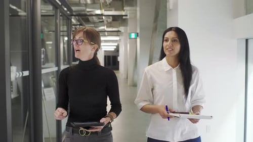 Businesswomen Walking And Talking In Modern Office Corridor