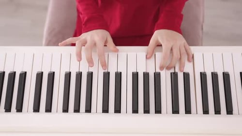 Close up of black white piano Keys being played by Hands of Young Child wearing Red Clothes. Aerial