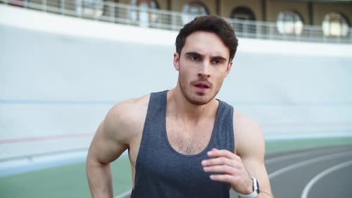 Exhausted young man runner doing running workout at modern stadium track outdoors