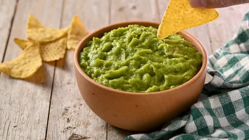 Tortilla Chip Dipping into Guacamole Bowl on Table