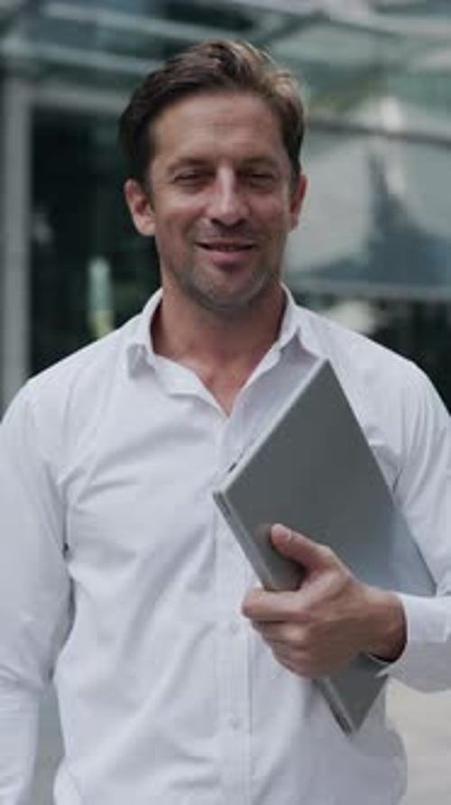 Portrait of Mature Businessman in Shirt Holds Laptop Near Office Building