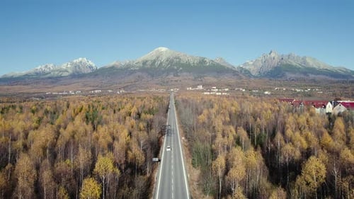Autumn drone shot of straight mountain road, view to high mountains, and forests.
