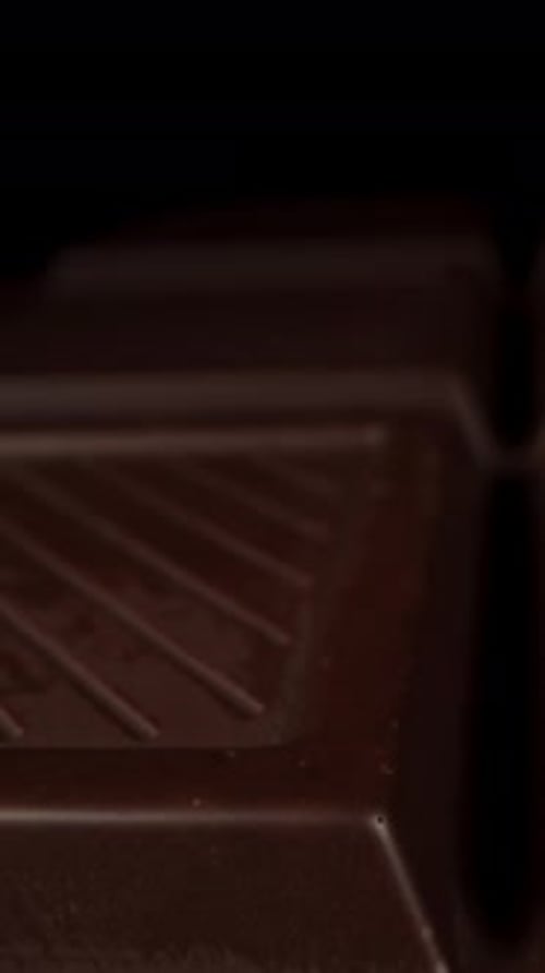 A black chocolate bar appears to levitate on a black background. Isolated. Vertical video.