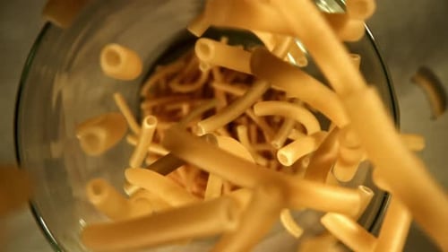 Raw pasta falling into clear bowl, close-up view