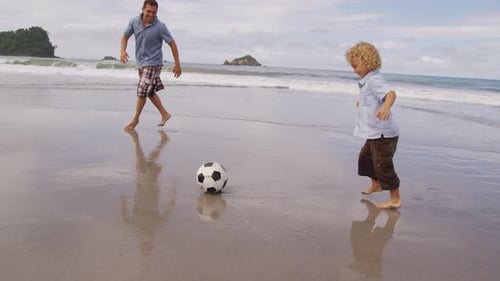 Padre e hijo jugando con un balón de fútbol en la playa. en rojo