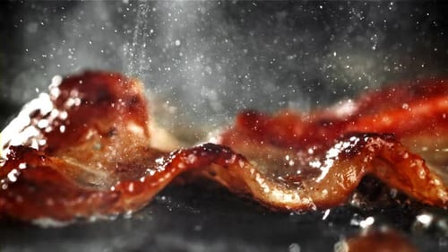 Crispy sizzling bacon cooking in hot pan closeup