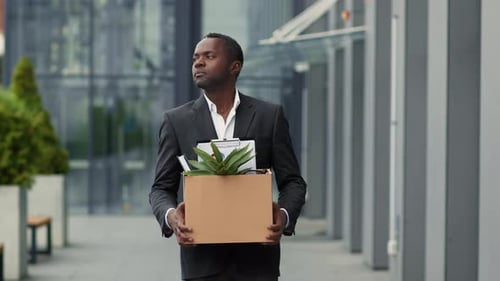 Follow Shot of Upset Middle Aged Black Employee Walking Near Office Building with Box with Personal