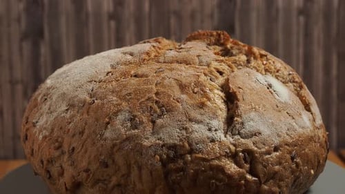 Rotation of dark bread on a wooden background. Round bread with grains. Close-up.