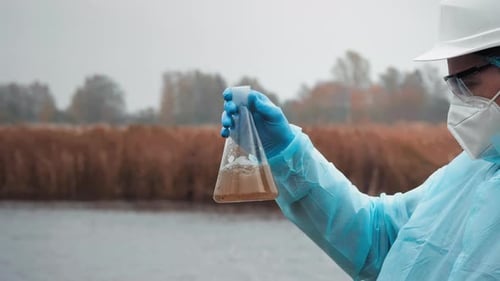 Scientist Shakes Sample in Flask by River