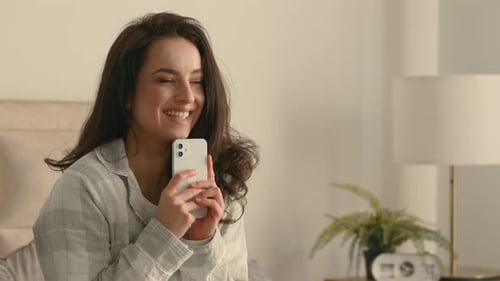 Woman Smiling and Using Cell Phone in Bed