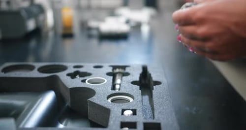 Female hands retrieve shiny engine parts from protective foam and assemble them.