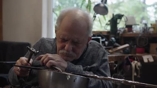 Elderly Master Craftsman on a Wheelchair Works in His Workshop Engraving Horimono Image on the Blade