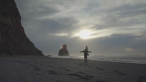 a person tourist walking on the sand of black beach towards rocks in the sea of Reynisfjall beach