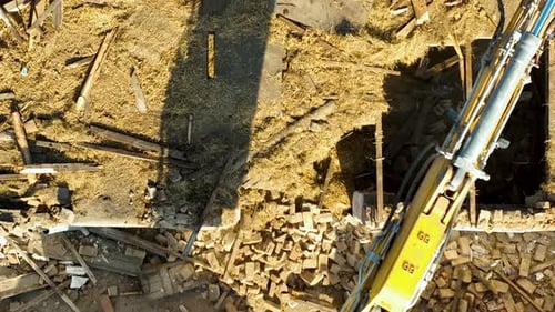 Vue aérienne d'un bras d'excavatrice manœuvrant au-dessus de débris, déblayant un chantier de construction pendant une opération