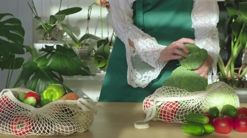 Mujer desempacando frutas y verduras de una bolsa ecológica sobre una mesa de cocina blanca en casa