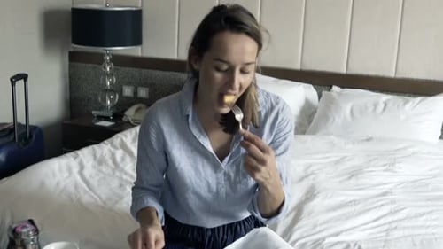 Young Pretty Businesswoman Eating Breakfast Sitting on Bed in Hotel 30s