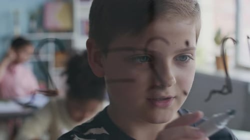 Young Boy Drawing On Glass In Class