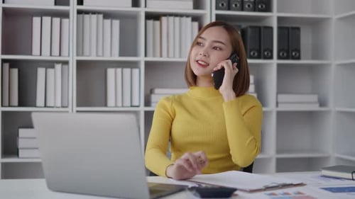 Businesswoman is talking to clients and colleague on the phone and working on laptop in office